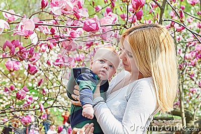 Mother walking with her baby son in garden of blooming magnolias Stock Photo