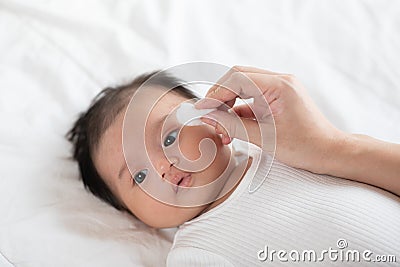 Mother is wiping the baby face with soft cotton, baby boy is lay down on the white mattress sheet . Being Parents are needed to Stock Photo