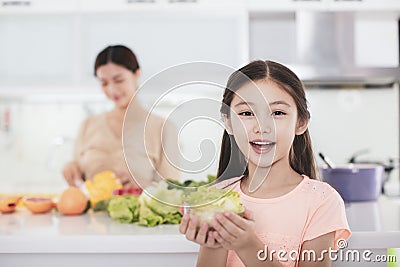 Mother working at kitchen and daughter showing health food Stock Photo