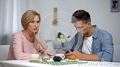 Mother worrying about adult son gadget addiction, male playing video game Stock Photo