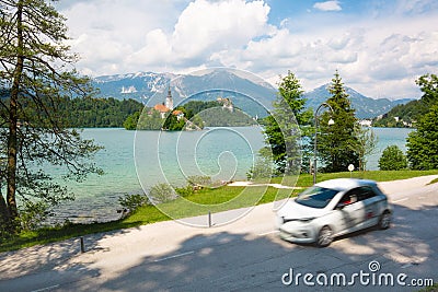 Motion blured white electric car in front of Bled lake, country of Slovenia. Travel, tourism, explore, rent a car Stock Photo