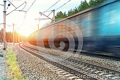 Motion blurred heavy cargo freight rusty train wagons moving on railway on sunset or sunrise day time. Industrial Stock Photo