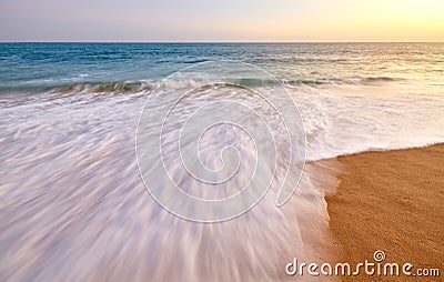 Motion blurred wave entering sandy beach at sunset Stock Photo