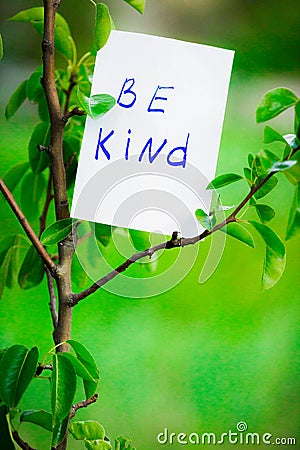 Motivating phrase be kind. On a green background on a branch is a white paper with a motivating phrase. Stock Photo