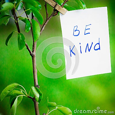 Motivating phrase be kind. On a green background on a branch is a white paper with a motivating phrase. Stock Photo