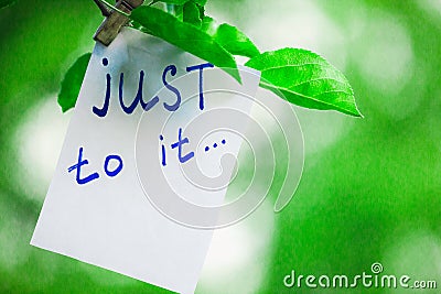 Motivating phrase just to it. On a green background on a branch is a white paper with a motivating phrase. Stock Photo