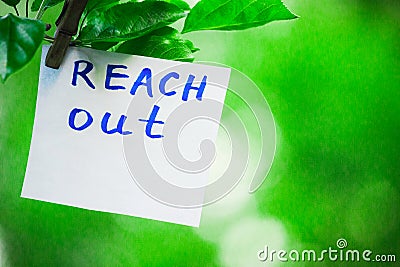 Motivating phrase reach out. On a green background on a branch is a white paper with a motivating phrase. Stock Photo
