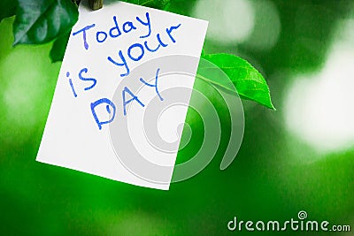 Motivating phrase today is your day. On a green background on a branch is a white paper with a motivating phrase. Stock Photo
