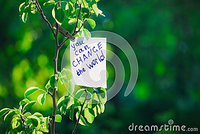 Motivating phrase You can change the world. On a green background on a branch is a white paper with a motivating phrase Stock Photo