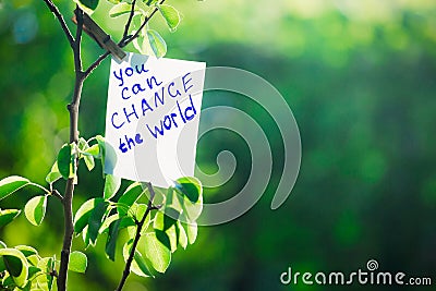 Motivating phrase You can change the world. On a green background on a branch is a white paper with a motivating phrase. Stock Photo