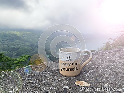 Motivational message on a coffee cup - Be easy on yourself. On mountain nature at misty morning background. Love yourself concepts Stock Photo