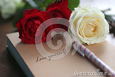 Motivational quote - Love yourself. Self love and care concept written on a book cover, with a pen, red and white roses background Stock Photo