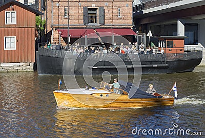 Motor boat floats on the river on the background of the summer cafÃ© of the ship. Old Porvoo, Finland Editorial Stock Photo