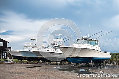 Motor boats stand on land under the open blue sky in the parking lot at the pier Stock Photo