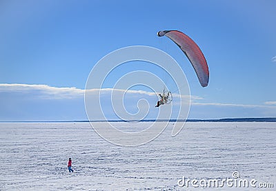 A motor paraplane flies over a frozen lake for a girl walking in the snow Editorial Stock Photo