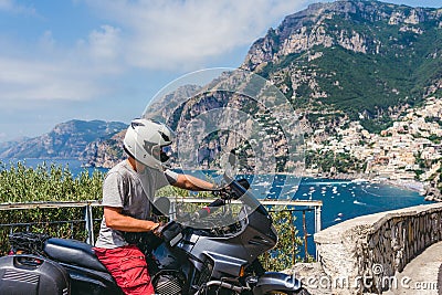 A motorbike traveler poses against the backdrop of an incredibly beautiful view of Positano, a city on the edge of cliffs, the sea Stock Photo