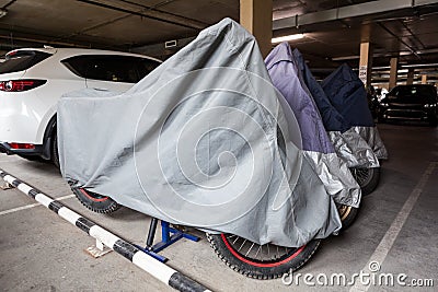 Motorcycles covered with safekeeping canvases standing in underground parking lot for winter keeping Stock Photo