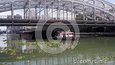 Motorized tugboat towing barge under the iron bridge on murky polluted Pasig River Stock Photo