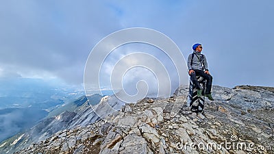 Mount Olympus - Man with helmet sitting on cloud covered mountain summit of Skolio peak on Mount Olympus Stock Photo