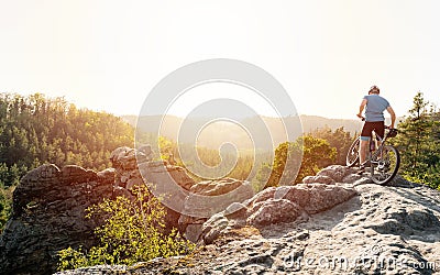 Mountain biker holding his bike on a rough cliff terrain on a sunset Stock Photo