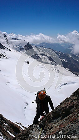 Mountain climber in silhouette climbing a steep rocky mountain peak high above white and wild glaciers with a great view behind hi Stock Photo