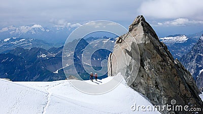 Mountain guide and client walk along a narrow snow ridge with a giant rock needle and a fantastic view behind t Editorial Stock Photo