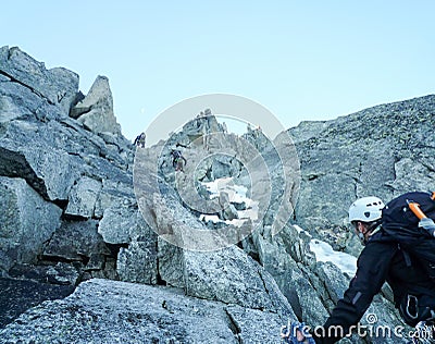 Mountain guide looking up on a rocky climb in the French Alps with rope teams ahead of him Stock Photo