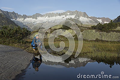 In a mountain lake the landscape is reflected. a hiker makes a break Stock Photo
