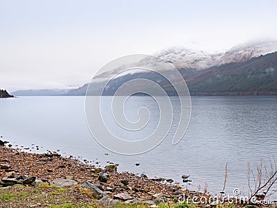 Mountain lake before misty sunset in Higland in Scotland. Snowy cone of mountain above mirroring water Stock Photo