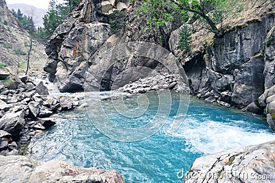 Mountain landscape with a waterfall and a rapid flow of icy blue mountain water Stock Photo