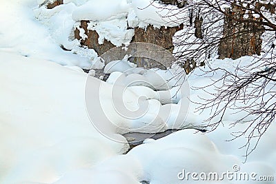 Mountain stream flows among the rocks and puffy white snow on the banks Stock Photo