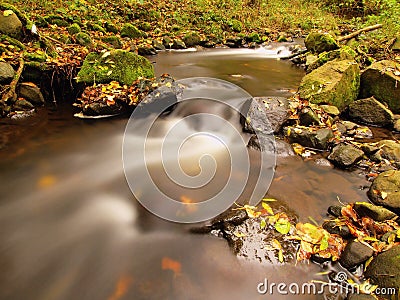 Mountain river with low level of water, gravel with first colorful leaves. Mossy rocks and boulders on river bank. Stock Photo