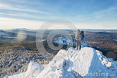 The mountaineer climbed the ice mountain top, man hiker standing at the peak of rock at sunrise. Stock Photo