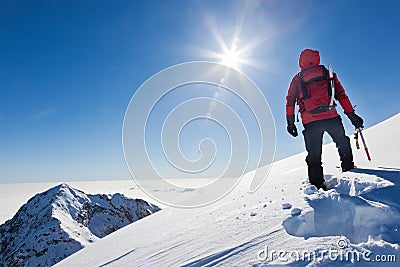 Mountaineer reaches the top of a snowy mountain in a sunny winter day. Stock Photo
