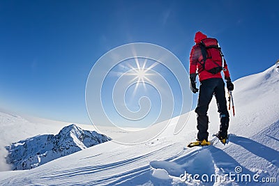 Mountaineer reaches the top of a snowy mountain in a sunny winter day. Stock Photo