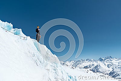 The mountaineer stands on the edge of the glacier with a snow shovel in his hands and shows Shak`s gesture against the Stock Photo