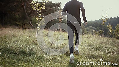 Mouvement lent Homme courant sur la colline grande d'herbe Vue arrière dépistant le tir L'appareil-photo suit le coureur de sport Mouvement lent Homme courant sur la colline grande d'herbe Vue arrière dépistant le tir L'appareil-photo suit le coureur de sport