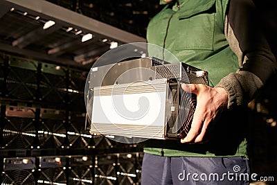 Mover holding bitcoin ASIC miner in warehouse. Worker with ASIC mining equipment on stand racks for mining Stock Photo