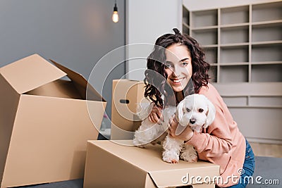 Moving to new apartment of young pretty woman with little dog. Chilling on bed surround carton boxes with pet, smiling Stock Photo