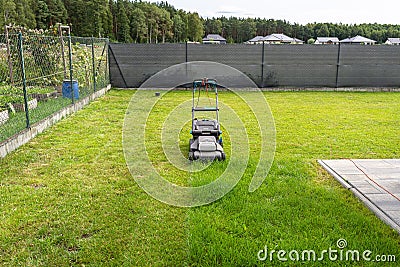 Mowing grass with an electric, powered mower, with a cutting width of 44 cm, visible mown rows. Stock Photo