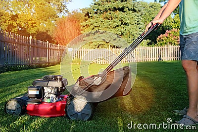 Mowing the grass with a lawn mower in sunny summer. Lawn mower season Gardener cuts the lawn in the garden. Stock Photo