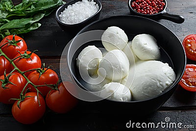 Mozzarella cheese balls, cherry tomatoes and green fresh organic basil peppercorns on wood table selective focus Stock Photo