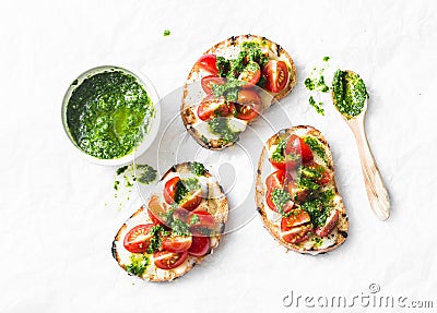 Mozzarella cheese, cherry tomatoes and arugula pesto bruschetta on light background, top view. Arugula pesto and sandwiches - tast Stock Photo