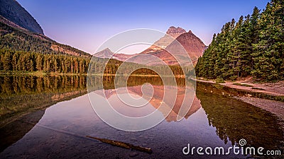 Mt. Wilbur reflection in the smooth surface of Fishercap Lake at sunrise in Glacier National Park Stock Photo