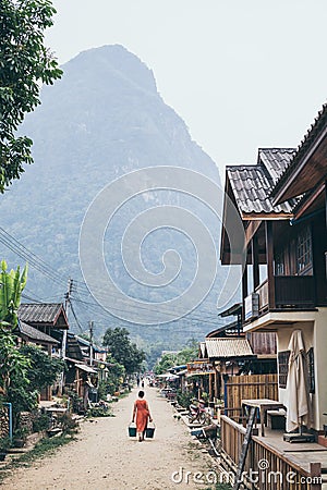 Muang Ngoi, Laos - May 2019: Laotian woman with two buckets walking on the central street of the village Editorial Stock Photo
