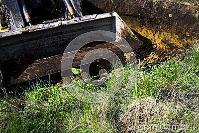 Muddy excavator bucket going to dig soil in grassy field in countryside Stock Photo