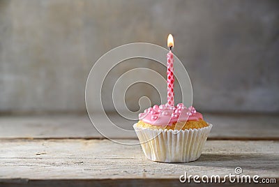 Muffin or cupcake with a pink burning candle on a wooden board against a rustic background, birthday concept with copy space Stock Photo