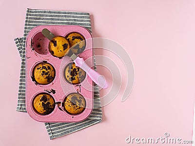Muffins in a pink cupcake shape, a kitchen spatula with a pink handle, a gray striped towel on a pink background. Stock Photo