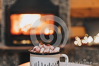 Mug of cocoa or hot chocolate with powdered marshmallows placed on a table by the fireplace Stock Photo