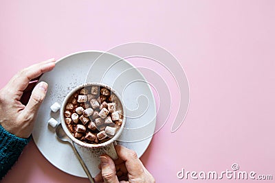 Mug with cocoa and marshmallows in female hands in knitted sweater on pink background. Top view. Stock Photo